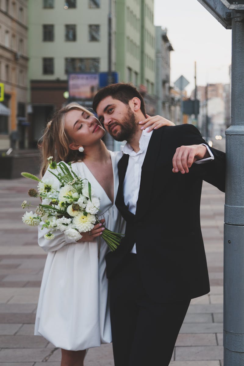 Elegant couple embracing on urban street, holding bouquet, perfect for wedding or romantic themes.