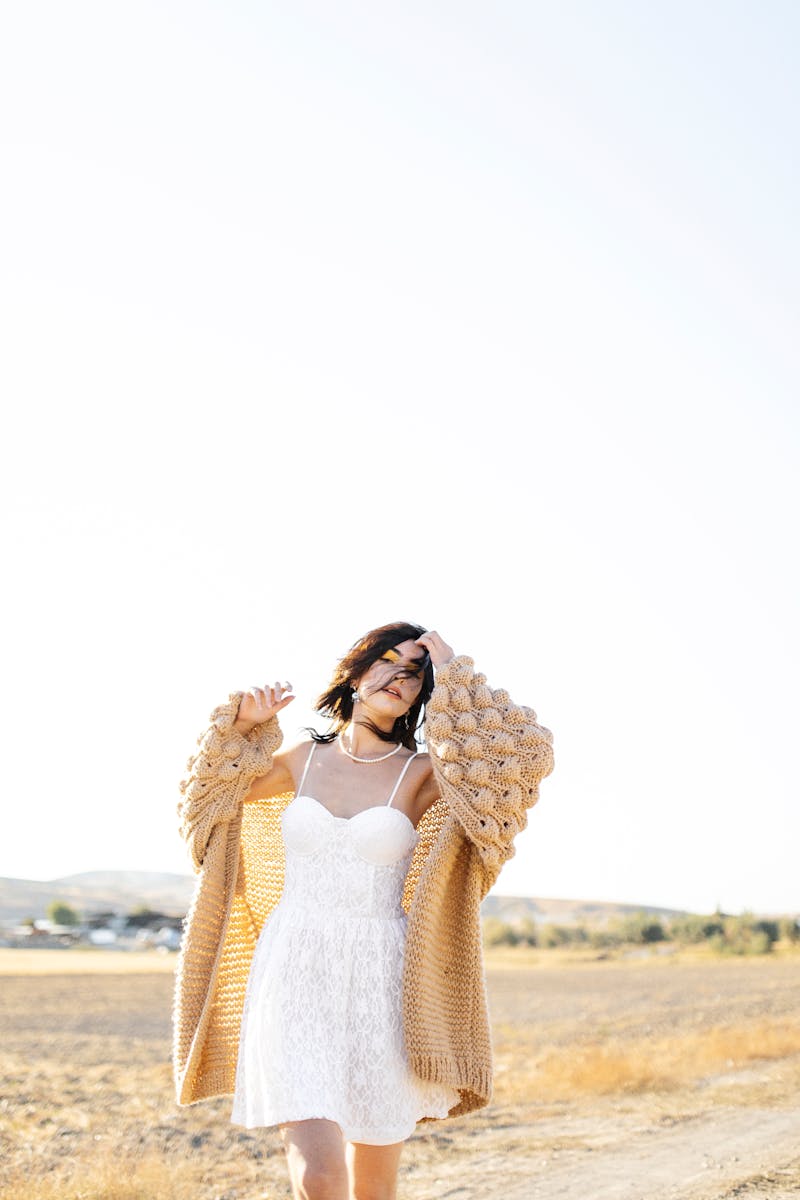 Woman in a white sundress with beige cardigan in a peaceful rural setting.
