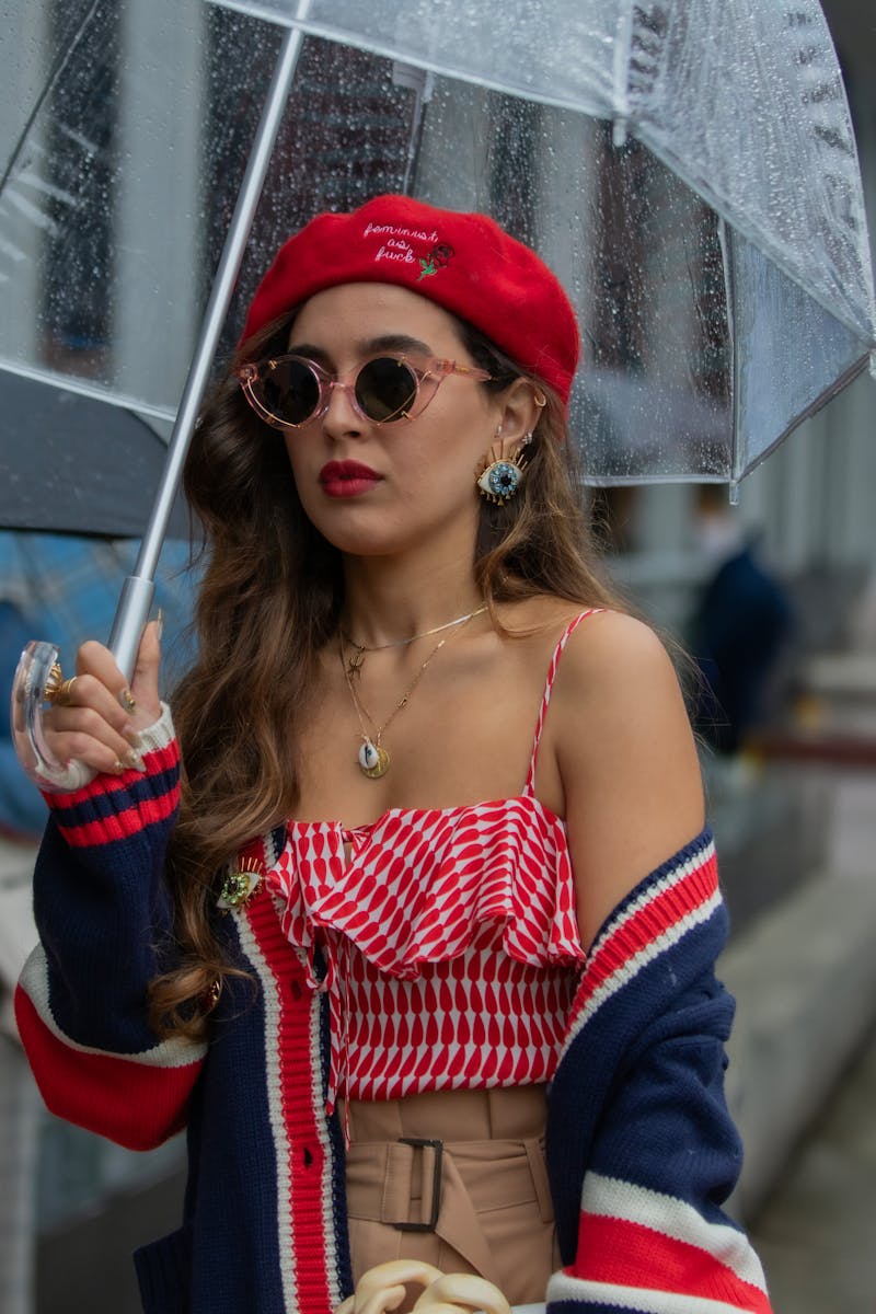 Stylish woman in trendy outfit with umbrella in city rain, emphasizing vibrant fashion.