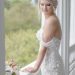 A bride in an exquisite lace gown stands gracefully on a balcony, embracing her special day.