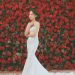 Bride in a white wedding gown posing against a vibrant red rose backdrop.