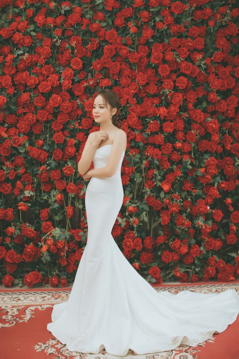 Bride in a white wedding gown posing against a vibrant red rose backdrop.