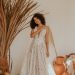 Bride in a lace gown poses with boho decor, exuding elegance and style.