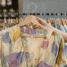 A person holding a vibrant patterned dress on a hanger inside a clothing store.
