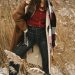 Woman models fashionable winter clothing in a snowy field, showcasing style and elegance.