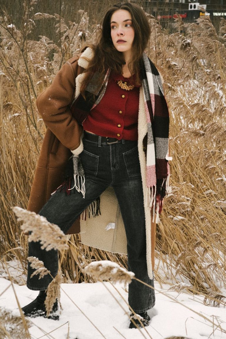 Woman models fashionable winter clothing in a snowy field, showcasing style and elegance.