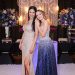 Two women in elegant evening gowns posing at a glamorous indoor event.