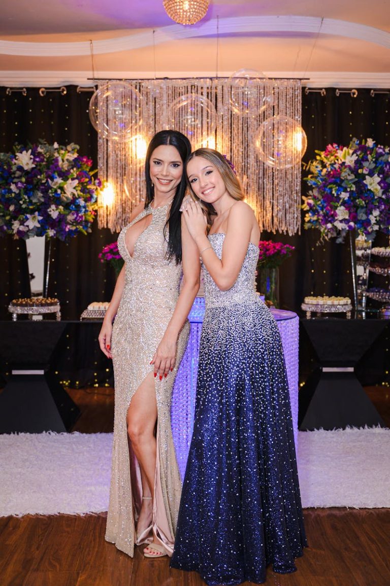 Two women in elegant evening gowns posing at a glamorous indoor event.