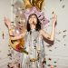 Joyous indoor celebration with balloons and confetti featuring a stylish young woman.