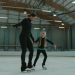 Woman and girl skating together in an indoor ice rink, practicing balance and technique.