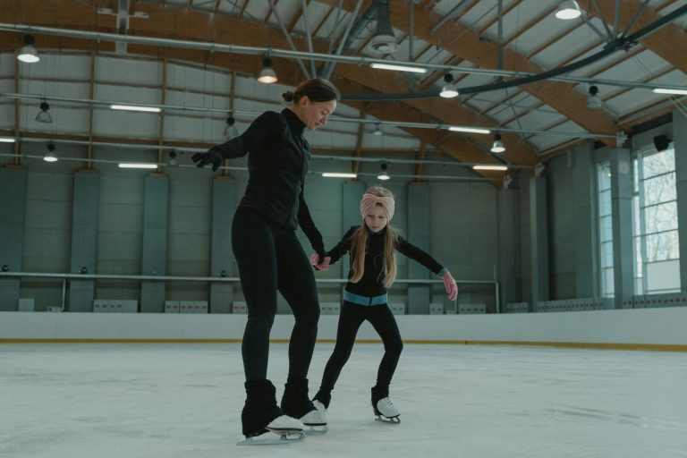 Woman and girl skating together in an indoor ice rink, practicing balance and technique.