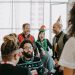 Group of coworkers celebrating holiday season in office with festive outfits and hats.