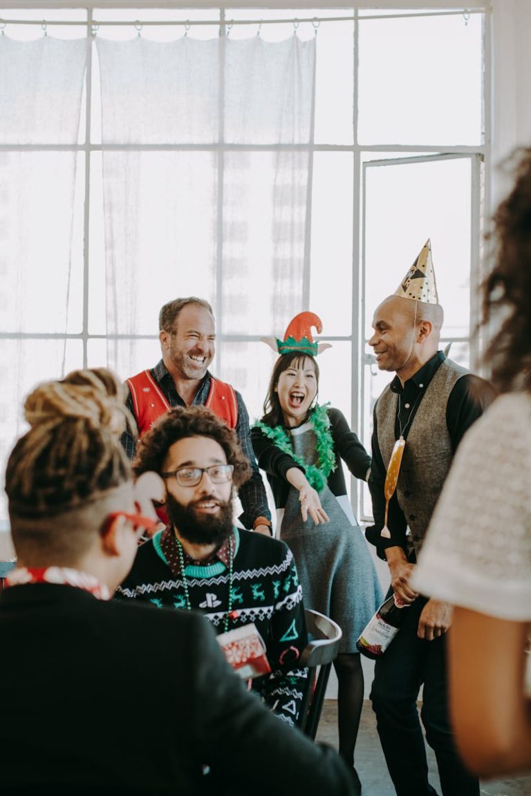Group of coworkers celebrating holiday season in office with festive outfits and hats.